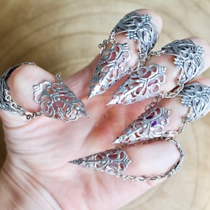 Op de afbeelding: Set van zes zilveren klauwringen met ingewikkelde filigraanontwerpen. De ringen zijn verbonden door delicate kettingen.