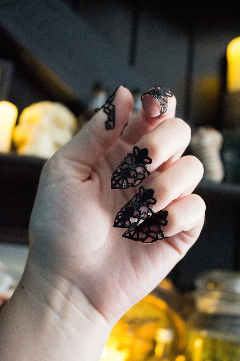 May include: Black lace fingertip rings, worn on a hand. The rings are delicate and intricate, with a pointed design.