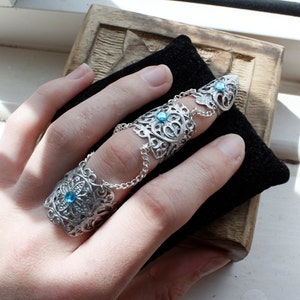 May include: A silver ring with a delicate filigree design and blue gemstones. The ring is designed to be worn on multiple fingers.