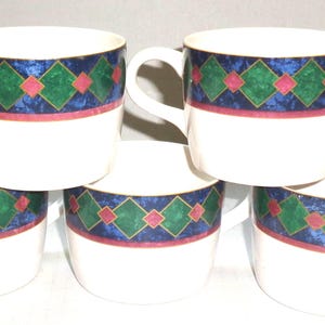 May include: A set of five white ceramic coffee mugs. Each mug features a decorative band with a blue background, green and red diamond pattern, and a gold trim. The mugs have a curved handle.