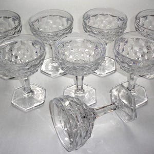 May include: A set of seven clear glass sherbet cups featuring a textured diamond pattern on the bowl and a hexagonal base. Six of the cups are standing upright in a triangular arrangement, while one cup is positioned lying on its side in front.