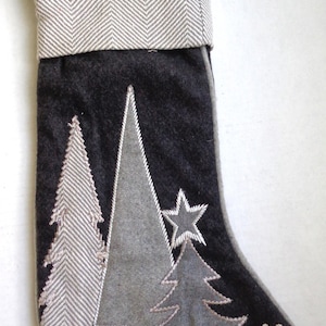 May include: A gray and white Christmas stocking with a gray felt background and white felt trees and a star. The stocking has a white and gray herringbone pattern cuff and three red and green plaid gift boxes.