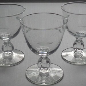 May include: Three clear glass goblets with etched floral designs. Each goblet has a rounded bowl, a decorative stem, and a circular base. The goblets are arranged in a triangular formation, showcasing their elegant design.