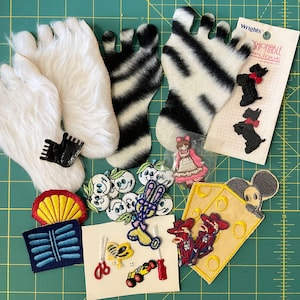 May include: A collection of assorted fabric appliques including two white faux fur feet, two zebra-striped feet, a Wrights brand card with two black dog patches, a yellow cheese wedge with a mouse, and various small embroidered motifs like flowers and tools.
