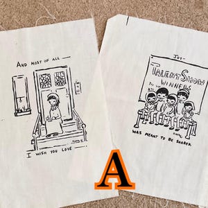 May include: Two off-white fabric panels with black ink illustrations. One shows a person on a porch with text "And most of all, I wish you love." The other depicts a talent show with text "Talent Show Winners" and "Was meant to be shared."