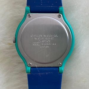May include: A close-up of the back of a Citizen watch with a blue and teal strap. The watch face is silver with the text "CITIZEN WATCH CO. WATER RESIST PLASTICS 8031-343662 KA JAPAN".