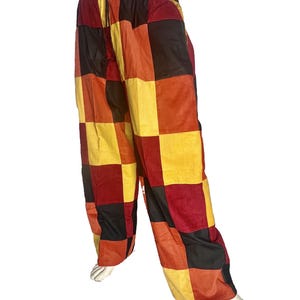 May include: Corduroy pants with a patchwork design in shades of red, yellow, orange, and black. The pants have a drawstring waist and a relaxed fit. The fabric appears to be soft and comfortable.