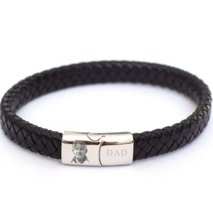 May include: Black leather braided bracelet with a silver clasp engraved with the word "DAD" and a photo of a man.