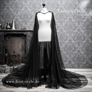 May include: A black tulle cape with beaded trim. The cape is draped over a white dress form. The text "Lucardis Feist Dark Couture" and "www.feist-style.de" are visible in the image.