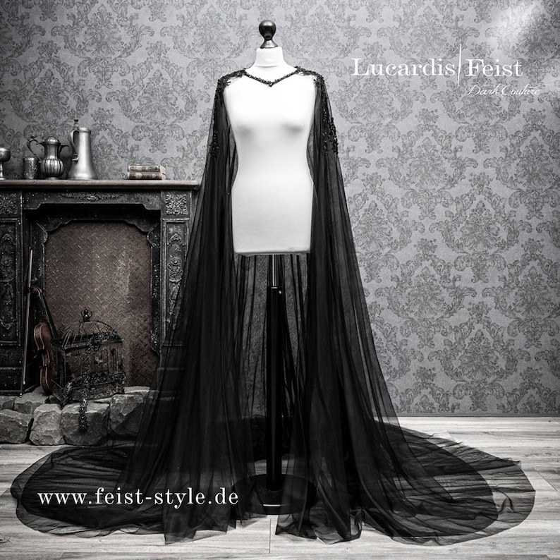 May include: A black tulle cape with beaded trim. The cape is draped over a white dress form. The text "Lucardis Feist Dark Couture" and "www.feist-style.de" are visible in the image.