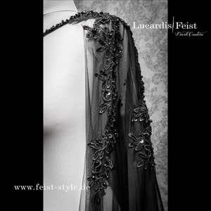 May include: Black sheer cape with black lace trim and bead embellishments. The cape is shown on a white mannequin. The text "Lucardis | Feist Dark Couture" and "www.feist-style.de" are visible on the image.
