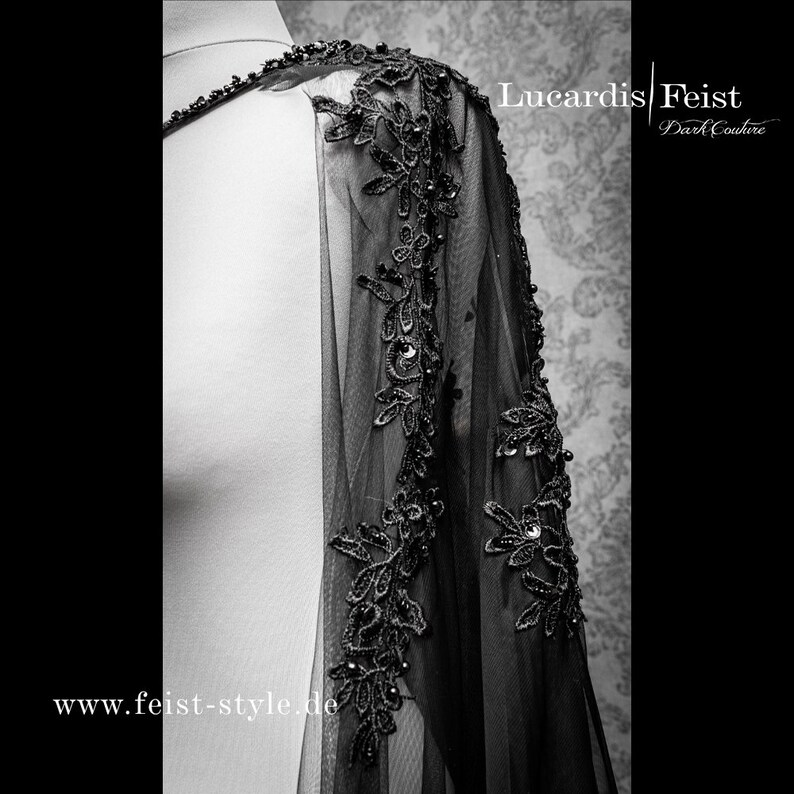 May include: Black sheer cape with black lace trim and bead embellishments. The cape is shown on a white mannequin. The text "Lucardis | Feist Dark Couture" and "www.feist-style.de" are visible on the image.