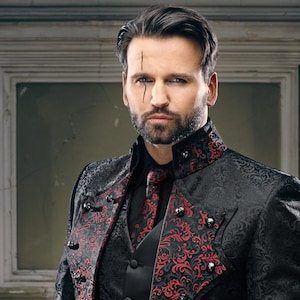 May include: A black jacket with a high collar and red floral brocade patterns on the lapels and cuffs. The jacket features small silver skull-shaped buttons along the front closure. A matching red and black patterned necktie is worn underneath.