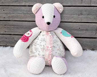 May include: A stuffed teddy bear constructed from various fabrics including lavender polka dot, white floral print, and striped patterns. The bear features small pink bows down the center, a pink owl patch on one arm, and a teal bird patch on the other.