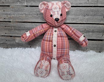 May include: A handmade teddy bear with a pink plaid pattern and white lace accents. The bear has black button eyes, a black nose, and a white lace trim down the center. The bear's paws and ears are also adorned with white lace.
