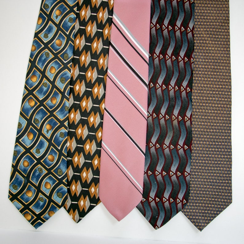 May include: Five neckties displayed side-by-side. The first features a blue grid with orange circles. The second has a black background with tan and white diamonds. The third is solid pink with diagonal white and black stripes. The fourth has wavy gray and maroon lines. The fifth is a tan and blue geometric pattern.