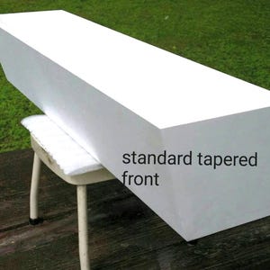 May include: A white, rectangular object with a tapered front, resting on a small stool. The text "standard tapered front" is visible on the side. The object appears to be made of a solid material, possibly wood or a similar substance.