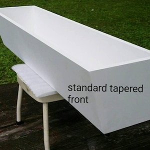 May include: White rectangular planter box with a tapered front. The planter is sitting on a white stool. The text "standard tapered front" is written on the planter.