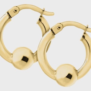 May include: A pair of gold-colored hoop earrings. Each earring features a rounded hoop design with a small, spherical accent in the center. The earrings have a polished, reflective surface, and a hinged clasp.