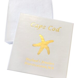 Puede incluir: Caja de joyer&iacute;a blanca con un dise&ntilde;o de l&aacute;mina dorada. La caja tiene el texto "Cape Cod" y "Michael's Jewelers Provincetown, MA" impreso en ella.