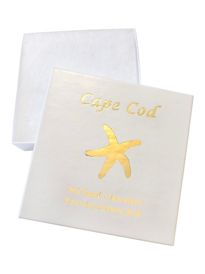 Puede incluir: Caja de joyer&iacute;a blanca con un dise&ntilde;o de l&aacute;mina dorada. La caja tiene el texto "Cape Cod" y "Michael's Jewelers Provincetown, MA" impreso en ella.
