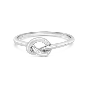 May include: A silver-colored ring with a knot design. The ring features a polished finish and a simple, elegant style. The knot is the focal point, creating a unique and eye-catching piece of jewelry.