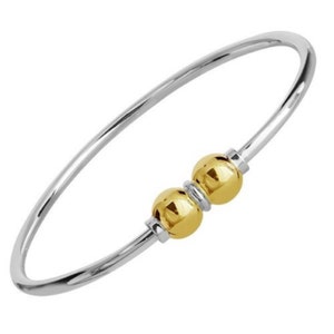 May include: A silver bangle bracelet with two gold beads. The bracelet is open and has a simple design.