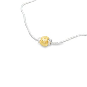 May include: A silver necklace with a gold-colored bead as a focal point. The bead is a rounded shape with silver accents on either side. The necklace has a delicate, snake chain design.