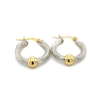 May include: A pair of silver hoop earrings with a gold ball accent. The earrings are twisted and have a textured finish.