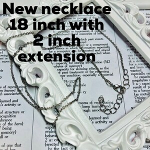 May include: A silver chain necklace with a 2 inch extension. The necklace is 18 inches long. The necklace is laying on a white surface with text in the background.