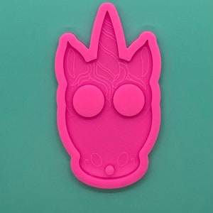 May include: Pink silicone mould shaped like a unicorn head with a swirl horn, two round eye cavities, and a small nose.