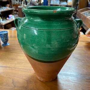 May include: A large green glazed ceramic pot with two handles. The pot has a brown rim and a brown band around the middle.