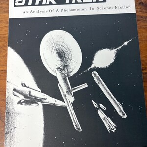 May include: Vintage Star Trek magazine cover featuring a black and white illustration of a spaceship and other spacecraft against a starry background. The magazine title is in bold white letters, with the text "An Analysis Of A Phenomenon In Science Fiction".