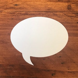 May include: A white speech bubble cut out of paper and placed on a brown wooden surface.