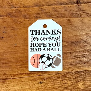 K&ouml;nnte beinhalten: Wei&szlig;er Dankesanh&auml;nger mit schwarzem Text, der "Danke f&uuml;rs Kommen! Ich hoffe, du hattest Spa&szlig;." lautet. Der Anh&auml;nger hat oben ein Loch und zeigt eine Grafik eines Basketballs, eines Fu&szlig;balls, eines Baseballs und eines Fu&szlig;balls.
