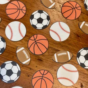 May include: A collection of colorful sports-themed paper circles, including basketballs, baseballs, footballs, and soccer balls. The circles are arranged on a wooden surface.