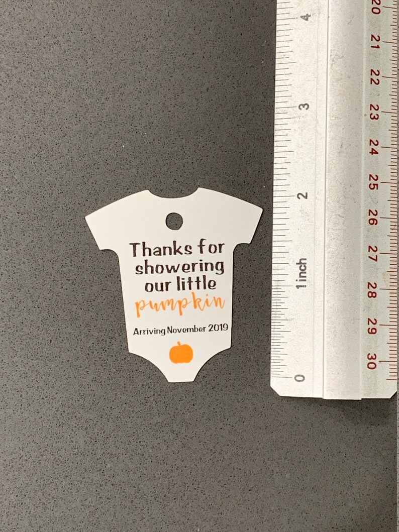 K&ouml;nnte beinhalten: Wei&szlig;er Baby-Strampler-f&ouml;rmiger Dankesanh&auml;nger mit dem Text "Danke, dass du unser kleines K&uuml;rbischen geduscht hast Ankunft im November 2019" und einer kleinen orangefarbenen K&uuml;rbisgrafik.