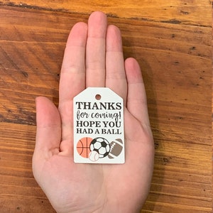 K&ouml;nnte beinhalten: Wei&szlig;er Dankesanh&auml;nger mit schwarzem Text, der "THANKS for coming! HOPE YOU HAD A BALL" lautet, mit einem Basketball, einem Fu&szlig;ball, einem Baseball und einem American Football.