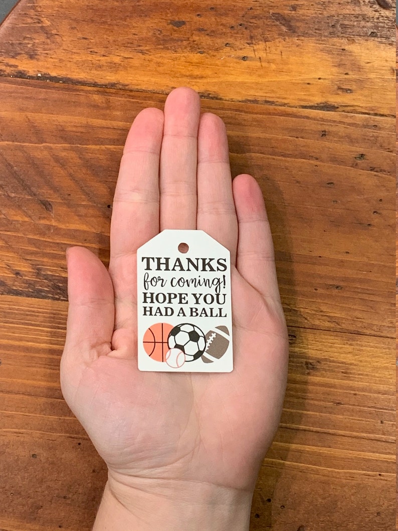 K&ouml;nnte beinhalten: Wei&szlig;er Dankesanh&auml;nger mit schwarzem Text, der "THANKS for coming! HOPE YOU HAD A BALL" lautet, mit einem Basketball, einem Fu&szlig;ball, einem Baseball und einem American Football.