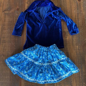 May include: A blue velvet long-sleeved shirt with a v-neck collar and a blue floral skirt with white lace trim.