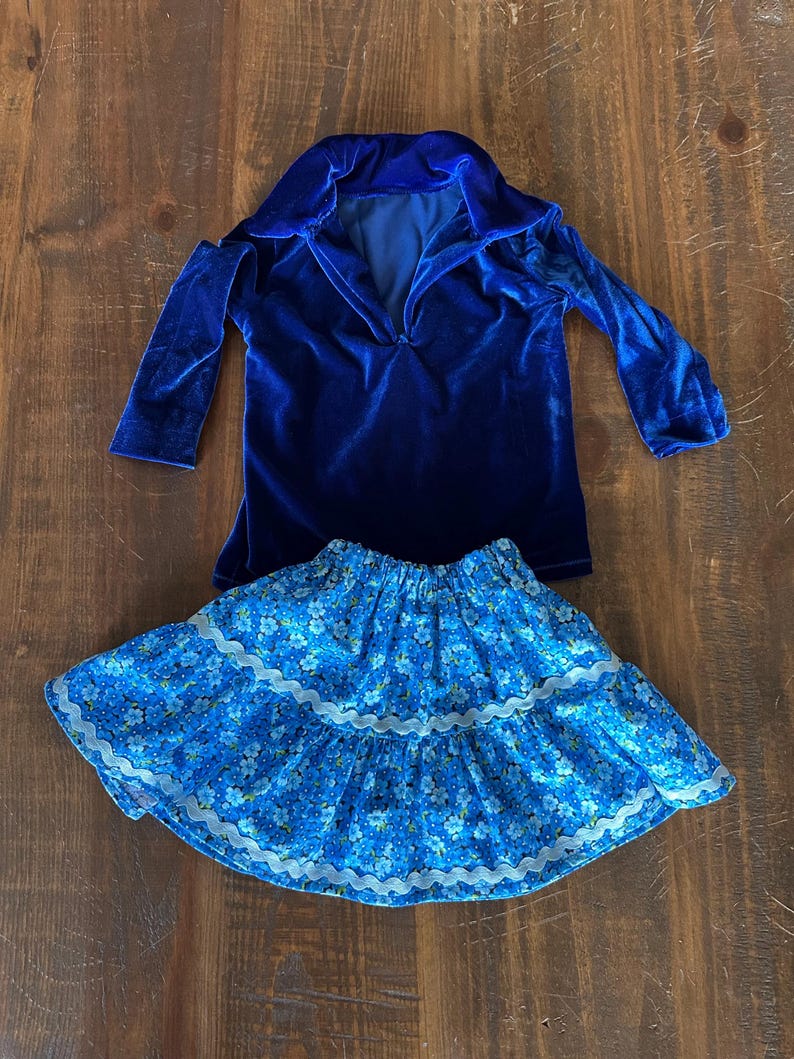 May include: A blue velvet long-sleeved shirt with a v-neck collar and a blue floral skirt with white lace trim.
