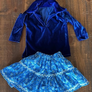 May include: A blue velvet long-sleeved shirt with a collar and a blue and white floral skirt with lace trim.