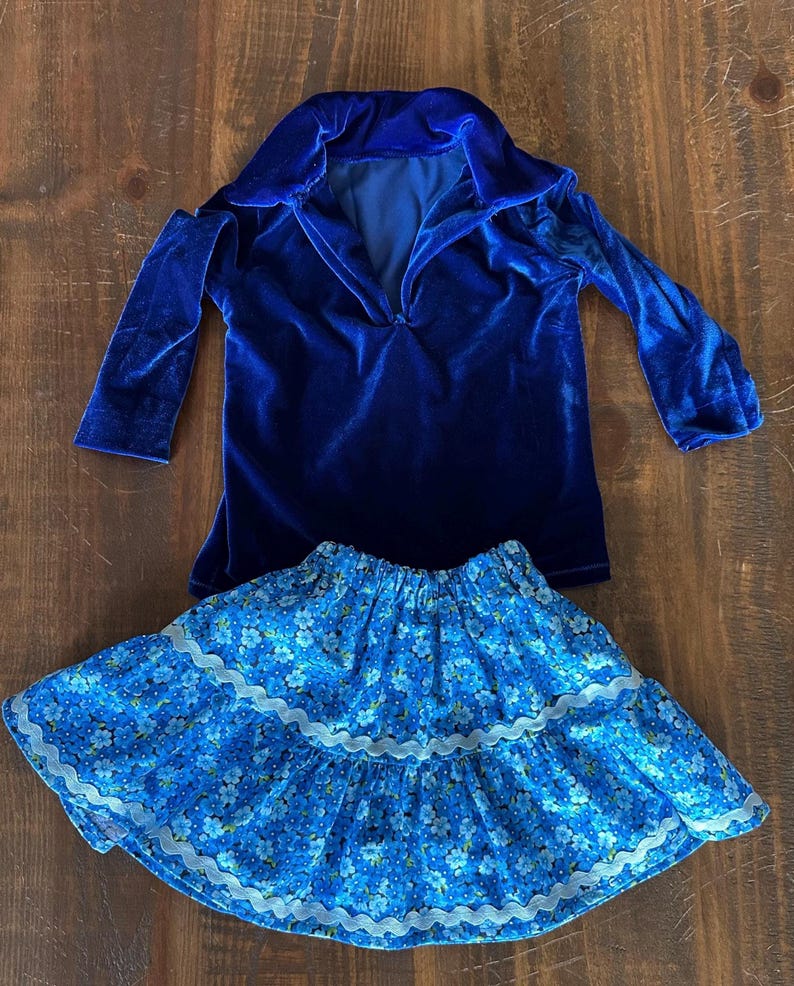 May include: A blue velvet long-sleeved shirt with a collar and a blue and white floral skirt with lace trim.