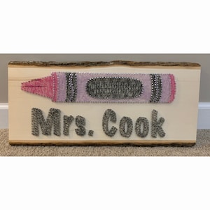 May include: A wooden sign with a string art design of a pink and black crayon and the text "Mrs. Cook".
