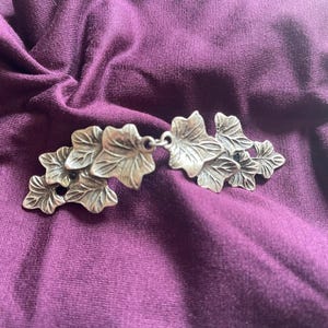 Peut inclure: Broche en métal argenté en forme de feuille de lierre. Les feuilles sont disposées en grappe et ont un aspect détaillé et réaliste.