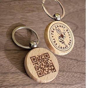 May include: Two wooden keychains with silver key rings. One keychain has a bee design with the text "The Lazer Bee Co.". The other keychain has a black and white QR code.
