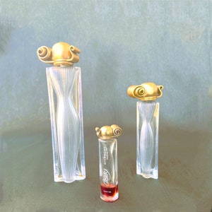 May include: Three glass perfume bottles with gold caps and labels. The bottles are different sizes and have a textured, ribbed design. The labels read "Givenchy Paris" and "Organza".