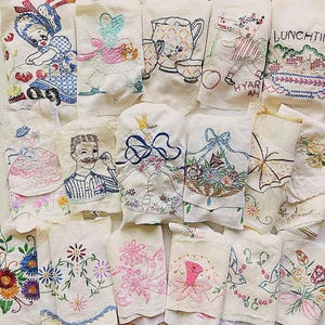 May include: A collection of vintage embroidered linen towels. Designs include floral patterns, figures, and kitchen scenes. Colors include blue, pink, green, and red. Some towels feature text, such as "Lunchtime" and "Hyar Ah."