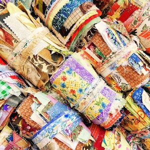 May include: Close-up of bundles of fabric scraps, tightly wrapped and tied. The fabrics display a variety of patterns, including floral, plaid, and geometric designs. The colour palette is diverse, featuring reds, blues, greens, and yellows, creating a patchwork aesthetic.