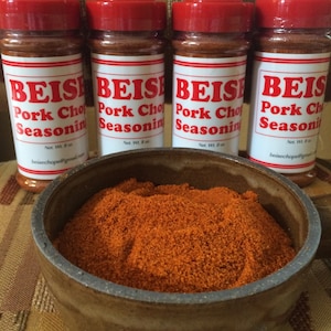 May include: Four red plastic jars of pork chop seasoning labeled "BEISE Pork Chop Seasoning" with a net weight of 8 oz. A brown ceramic bowl filled with red seasoning.